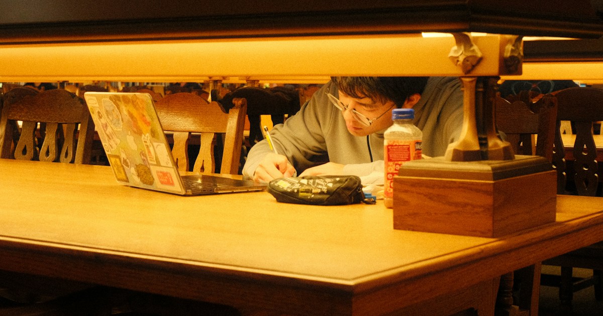 A student taking notes beside a laptop in a library
